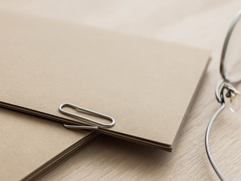 Close-up of a paper clip on a closed manila folder, with reading glasses beside it.